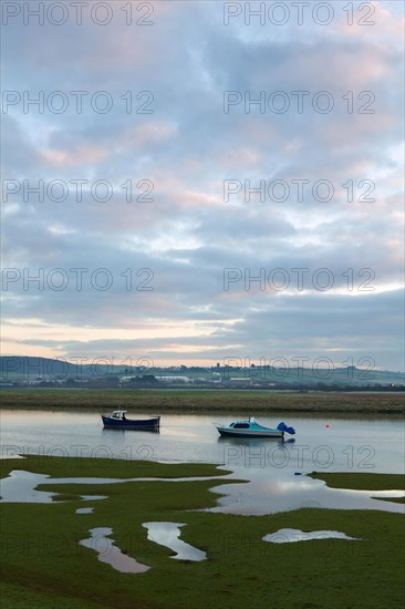 Two small boats rising with incoming tide on tidal stretch of river at dawn