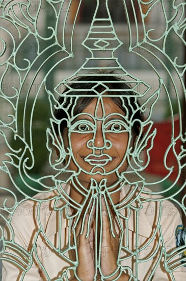 Young Khmer woman looking through a metal lattice gate with a Buddha figure