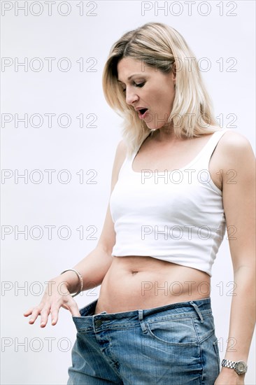 Young woman wearing too large jeans and looking surprised at her slim belly