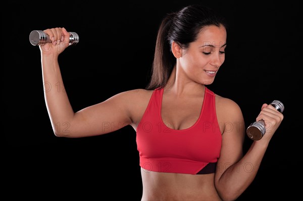 Young woman wearing a red sports bra while doing fitness training with chrome dumbbells