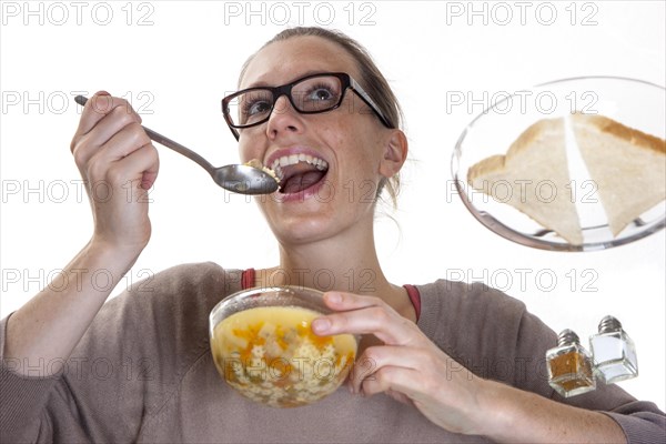 Young woman sitting at a glass table eating clear vegetable soup