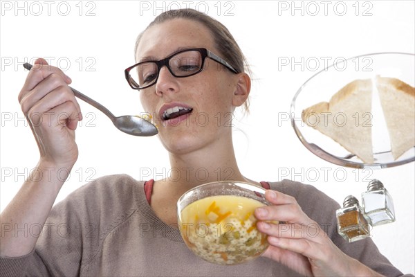 Young woman sitting at a glass table eating clear vegetable soup