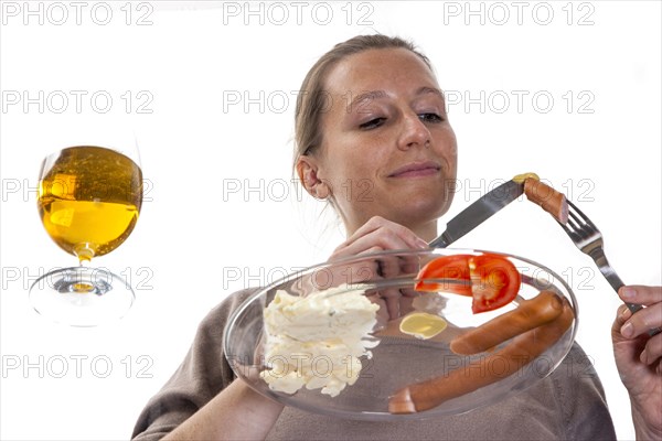 Young woman sitting at a glass table eating Frankfurter sausages with potato salad