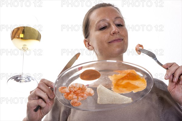 Young woman sitting at a glass table eating a cold fish dish