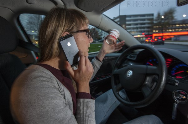 Young woman driving a car in the city centre while talking on her cell phone and holding a cup of coffee at the same time