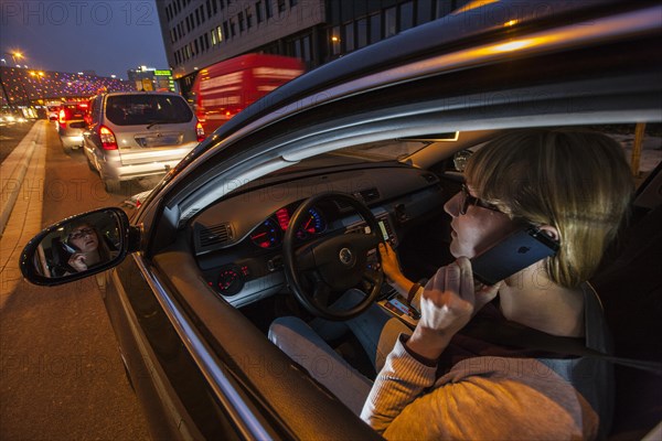 Young woman driving a car in the city centre in the evening while talking on her cell phone