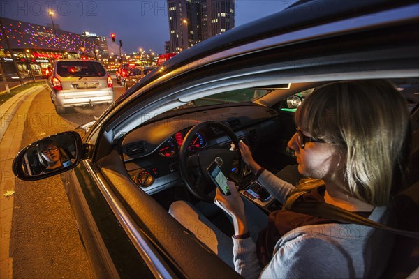 Young woman driving a car in the city centre in the evening while texting on her cell phone