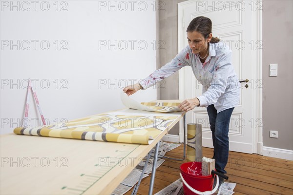 Young woman preparing wallpaper for wallpapering the walls