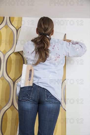 Young woman wallpapering a wall