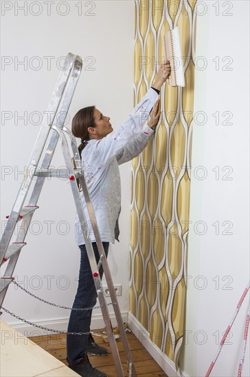 Young woman wallpapering a wall