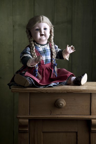 Antique doll sitting on a small chest of drawers