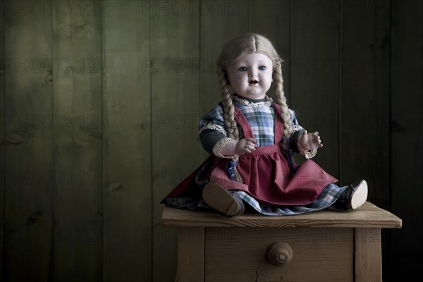 Antique doll sitting on a small chest of drawers