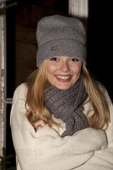 Smiling young woman wearing a cap and a scarf standing in front of a hiking hut