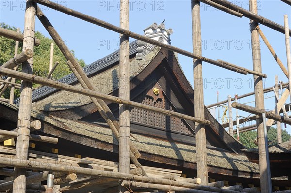 Shrine building is surrounded by scaffolding consisting of long logs