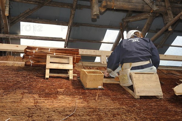 A roofer with a hard hat is nailing cypress bark to the roof of the Kamigamo Shrine