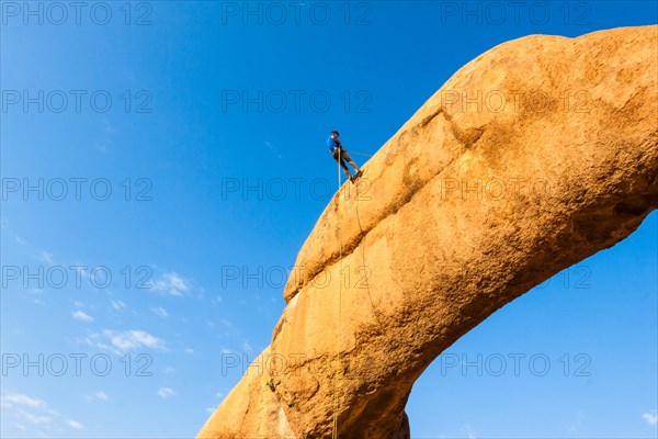 Young man abseiling from a rock arch