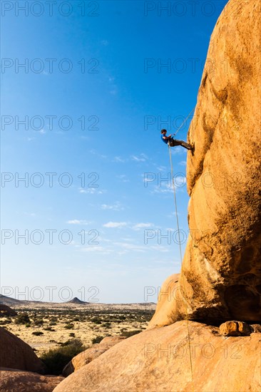 Young man abseiling from a rock arch