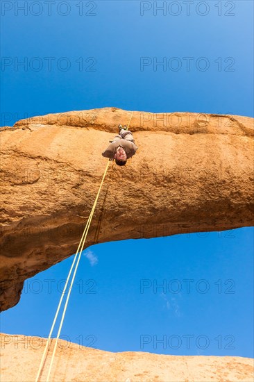 Young man abseiling from a rock arch