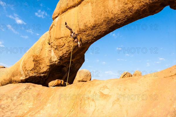 Young man abseiling from a rock arch