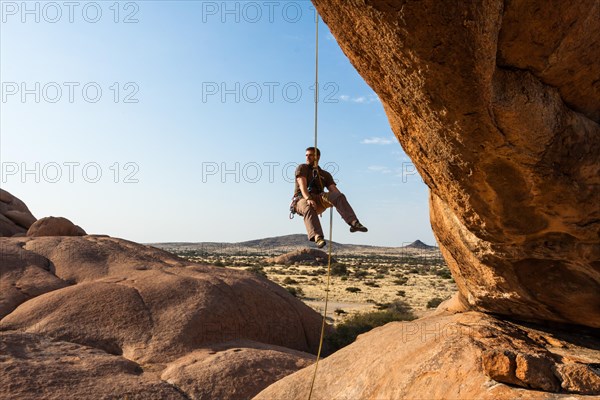 Young man abseiling from a rock arch