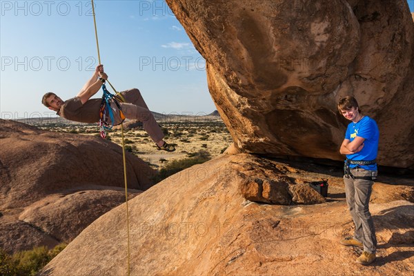 Young man abseiling from a rock arch