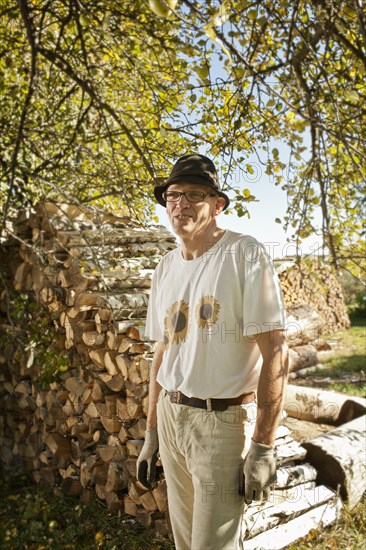 Man in the orchard in front of a wood pile