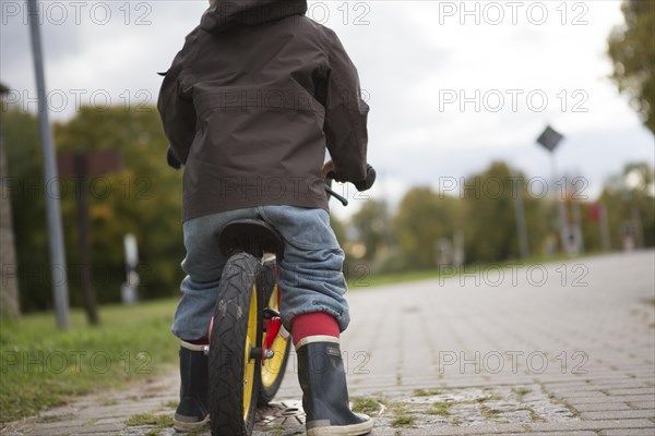 A young boy is practicing to ride a bicycle on a quiet street