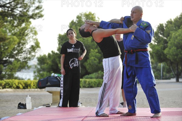 A martial arts instructor is demonstrating a defensive move on a student in a park