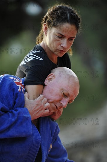 Woman is holding a man in a headlock during a martial arts training session in a park