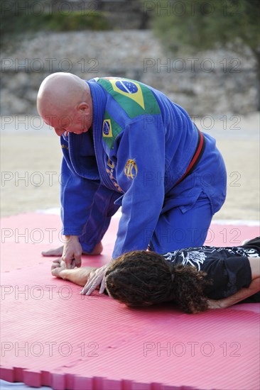 A martial arts instructor is teaching a grip to a student on a mat in a park