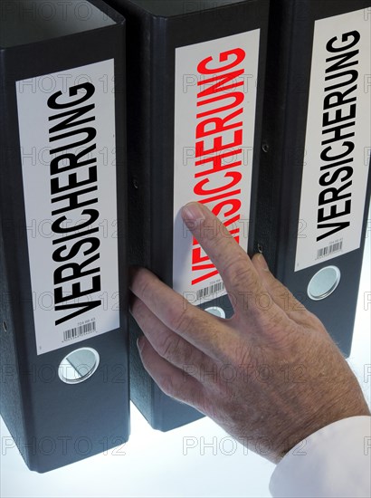 Hand reaching for a ring binder labelled 'VERSICHERUNG'