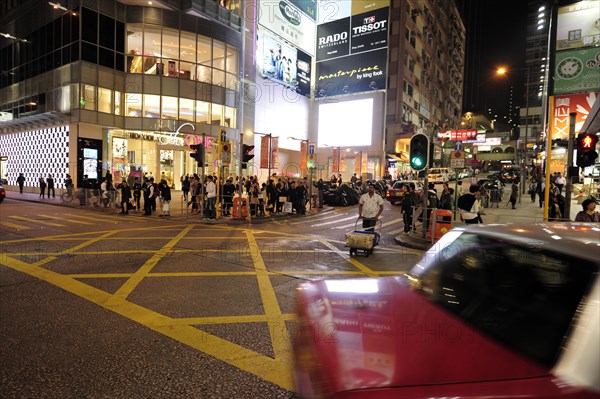 A red taxi driving on a street in Tsim Sha Tsui in the evening