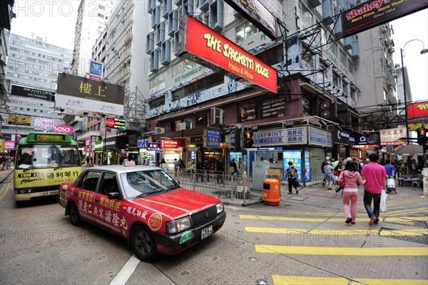 A red taxi waiting at a zebra crossing on a street in the Tsim Sha Tsui district