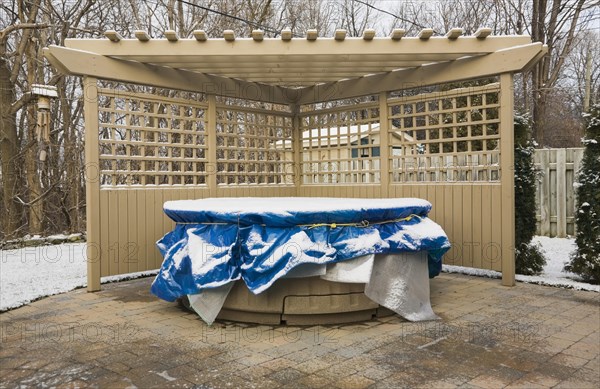 Wooden pergola and a spa in a residential backyard covered up for the winter season