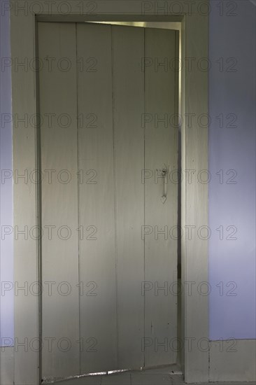 Partially opened wooden guest room door on the upstairs floor of an old Canadiana cottage style wooden siding residential home