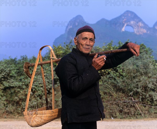 Man carrying a load with a shoulder pole in front of Moon Mountain near Yangshuo
