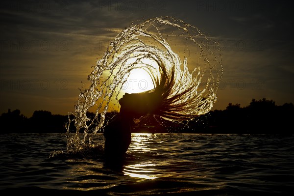 Young woman standing in the sea throwing back her long hair with splashing water