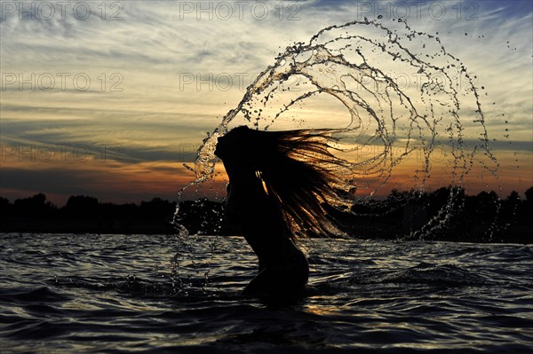 Young woman standing in the sea throwing back her long hair with splashing water