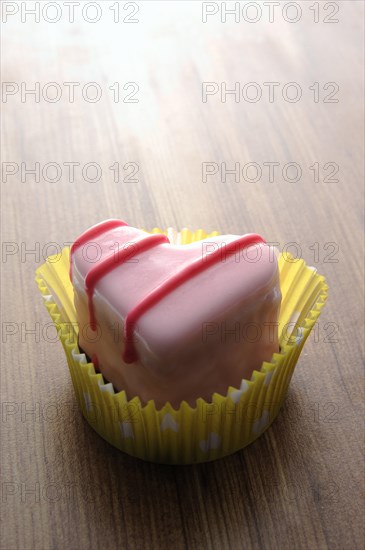 Pink heart-shaped petit four on a wooden surface