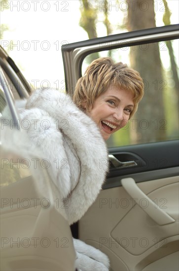 Laughing woman with a fur coat getting out of a car