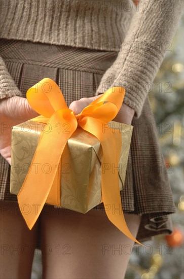 Woman in a mini skirt is holding gift wrapped in golden paper