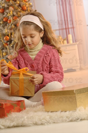Girl unpacking a gift in front of a Christmas tree