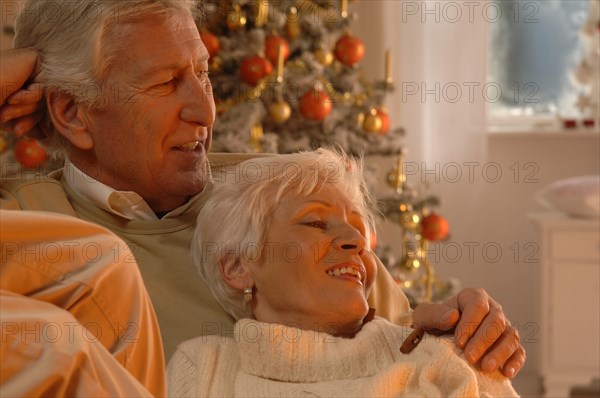 Mature couple in love sitting on a sofa in front of a Christmas tree