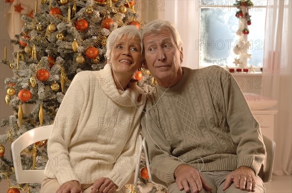 Mature couple with headphones sitting in front of a Christmas tree