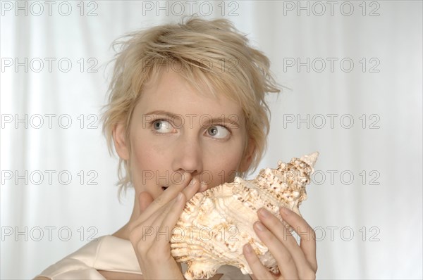 Young woman holding large shell to her mouth