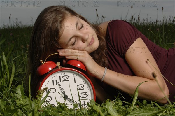 Teenage girl lying on the grass and sleeping on an oversized alarm clock