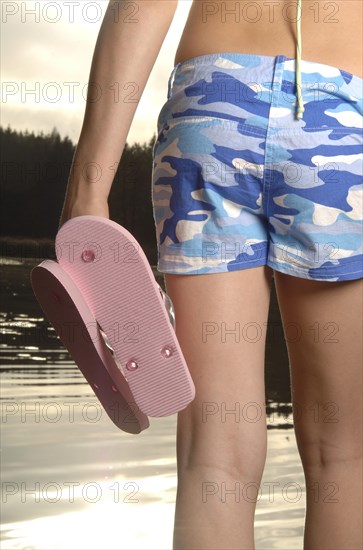 Teenage girl walking beside a lake with flip flops in her hand