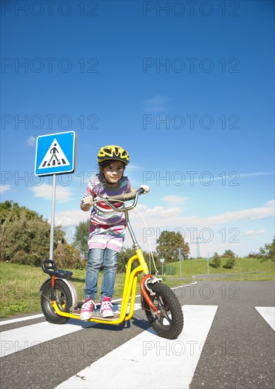 Girl crossing a zebra crossing with her scooter