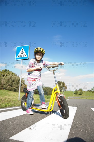 Girl crossing a zebra crossing with her scooter