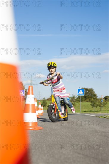 Girl practicing to ride slalom on a scooter at a traffic awareness course